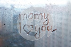 Foggy glass on window with written finger word momy i love you with heart shape on blue overcast wet window