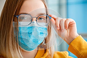 Foggy glasses wearing on young woman. close up portrait. Teenager girl in blue medical protective face mask and eyeglasses wipes