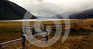 Foggy lake and mountains and farm with withered grass and zigzag fence