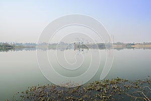 Foggy lake near modern city at sunny winter noon