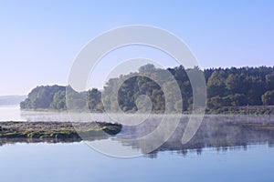 Foggy landscape with tree silhouette and reflection on water on fog at sunrise.Early summer morning on tranquil lake.Morning