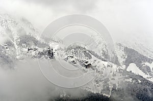 A foggy misteric panoramic view of the Alps mountains partially covered with the snow on a cloudy October