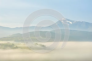 Foggy morning with forest and mountain silhouettes. Warm summer nature background.