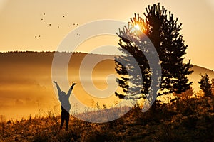 Foggy morning in the hills. The silhouette of a girl happily tossing flowers in the air. Beautiful golden sunrise