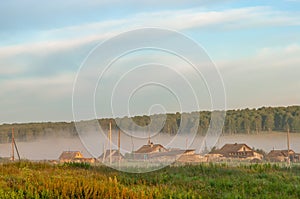 Foggy morning in a rural landscape. wooden village houses in fog and sunbeams