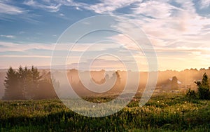 Foggy morning in a rural landscape. wooden village houses in fog and sunbeams