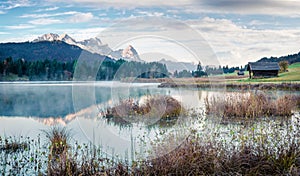 Foggy morning scene of Wagenbruchsee Geroldsee lake with Zugspitze mountain range on background. Beautiful autumn view of