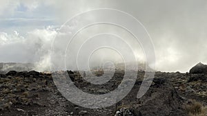 Foggy mountain landscape. Broken stones and boulders. Campground in the distance. Climbing Kilimanjaro, Africa