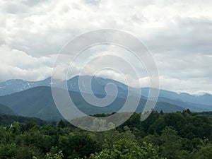 Foggy mountain peaks and hills with forest in front