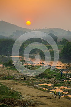 Foggy red sunset over river with African people walking and washing, Nigeria, Africa