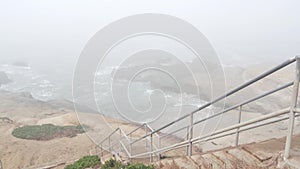 Foggy sea landscape, wave crashing on ocean beach, stairs in haze, misty weather