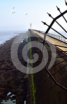 A foggy seascape with a sunlit pier and a lighthouse