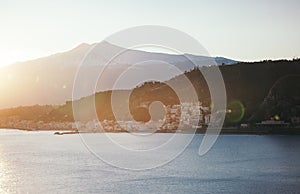 Foggy silhouette of of Etna volcano and a Sicilian village in the Naxos Bay - view from sea at sunrise, Sicily