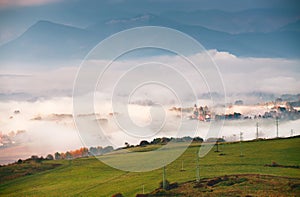 Foggy sunny morning in mountain village. Misty hills