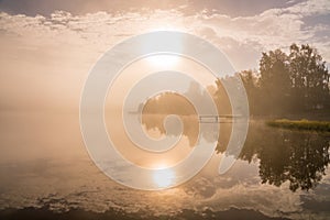 Foggy sunset with forest at long coast line, golden calm lake, Swedish countryside