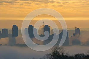 Foggy view of the morning city. Fiery dawn in Kiev. Buildings in the fog