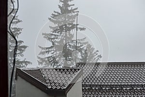 Foggy weather over a metal shingle covered rooftop of a house in the misty mountains