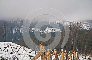 Foggy winter landscape - snowy glade with wood fence and foggy forest landscape in the background