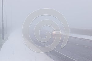 Foggy winter road, cars driving fading into the fog