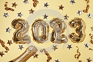 Foil gold air balloons in the form of number 2023 on yellow background with confetti stars and party streamers.