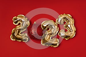 Foil gold air balloons in the form of numbers 2023 with red shiny Christmas bauble on red background. New year and