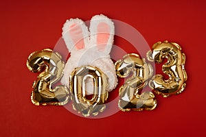 Foil gold air balloons in the form of numbers 2023 with simbol of year of the rabbit's ears on red background.