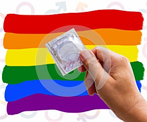 Foil pack of condom in man hand and colors of the rainbow LGBT background. The concept of safety from sexually transmitted