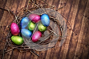 Foil wrapped colourful easter eggs in pink, green, blue and yellow in a natural nest made of sticks and twigs.