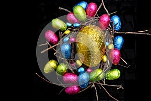 Foil wrapped multi coloured easter eggs in pink, green, blue and yelow in a natural nest made of wood, sticks and twigs.