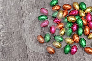 Foil wrapped multi coloured easter eggs in pink, green, orange and yellow in a pile or group, against a grey white wooden