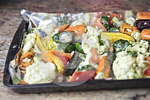 Foiled lined baking sheet filled with raw carrots, cauliflower,