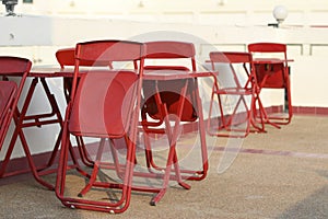 Foldable red table and chair set placed outdoors. Foldable chairs, leaning on the table.