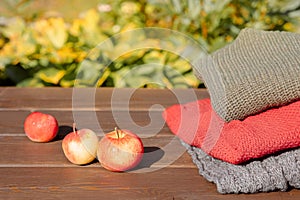 Folded autumn and winter clothing. Pile of knitted cashmere sweaters with apple on wooden table. Autumn composition on