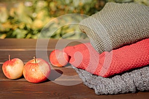 Folded autumn and winter clothing. Pile of knitted cashmere sweaters with apple on wooden table. Autumn composition on