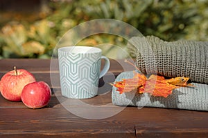 Folded autumn and winter clothing. Pile of knitted cashmere sweaters with maple leaf, apple and cup of tea on wooden