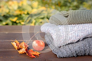 Folded autumn and winter clothing. Pile of knitted cashmere sweaters with maple leaf and apple on wooden table. Autumn