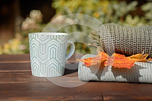 Folded autumn and winter clothing. Pile of knitted cashmere sweaters with maple leaf and cup of tea on wooden table