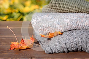 Folded autumn and winter clothing. Pile of knitted cashmere sweaters with maple leaf on wooden table. Autumn composition