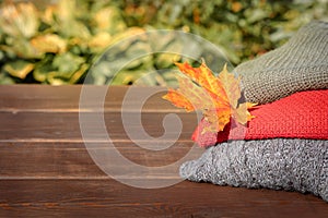 Folded autumn and winter clothing. Pile of knitted cashmere sweaters with maple leaf on wooden table. Autumn composition