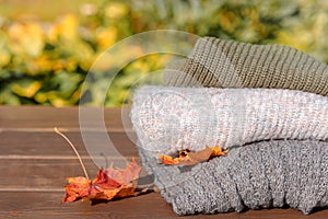 Folded autumn and winter clothing. Pile of knitted cashmere sweaters with maple leaf on wooden table. Autumn composition