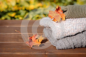 Folded autumn and winter clothing. Pile of knitted cashmere sweaters with maple leaf on wooden table. Autumn composition