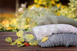 Folded autumn and winter clothing. Pile of knitted cashmere sweaters with maple leaf on wooden table. Autumn composition