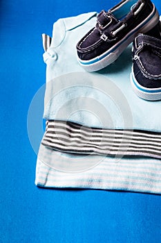 Folded blue bodysuit with boat shoes on it on minimalistic blue background. diaper for newborn boy. Stack of infant clothing. Chil