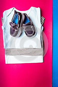 Folded blue bodysuit with boat shoes on it on minimalistic pink and blue background. diaper for newborn boy. Stack of infant cloth