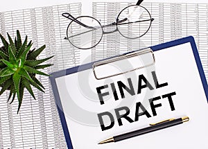 Folded business papers, pen, glasses, a flower in a pot and a tablet with a sheet of paper with the text FINAL DRAFT on the