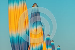 Folded colorful beach umbrella parasols on Adriatic sea coast in sunny summer morning, holiday and vacation background with copy