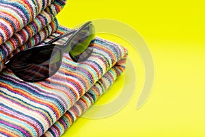 Folded Colorful Striped Organic Cotton Beach Towels and black Sunglasses on bright yellow as Summer Vacation Theme.