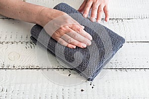 Folded grey towel on a white wooden table near woman`s hands. Spa and wellness, cotton terry textile. Ecological theme.