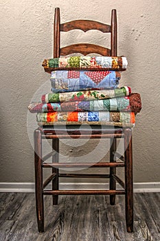 Folded handmade quilts resting on a ladder back chair