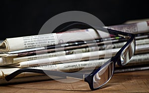 Folded pile newspapers with a pair of blue reading glasses on it